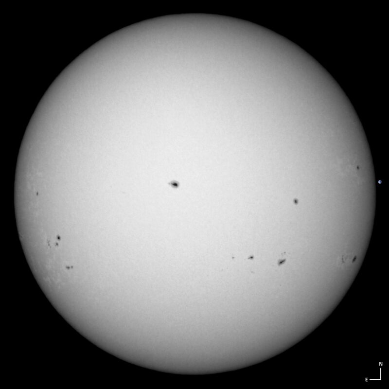 The sun, seen as a large white sphere with small dark spots.