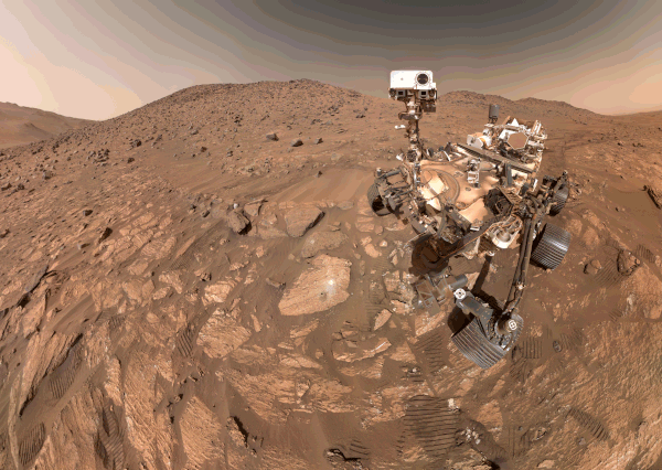 Selfie of robotic rover looking down at a rock with drill holes.