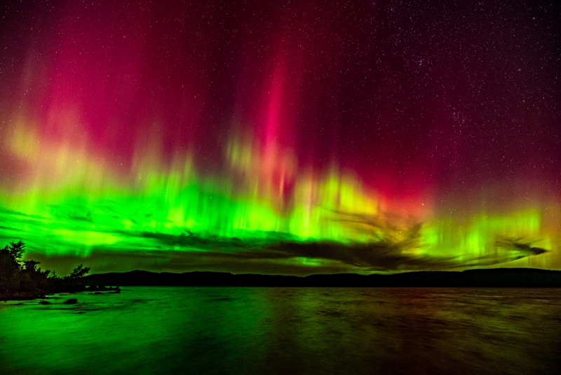 Over a wide expanse of water at night, vivid green in the sky gives way to streaks of crimson.