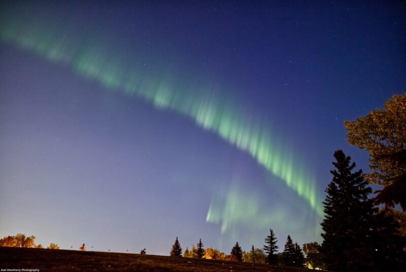 A green line of light crossing a dark blue sky.