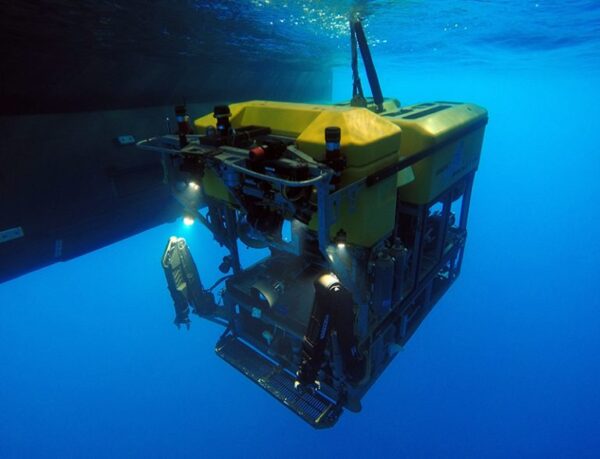 Square machine with robotic arms and lights underwater.