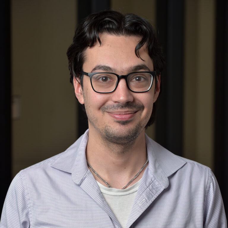 Smiling young man with dark hair and glasses.