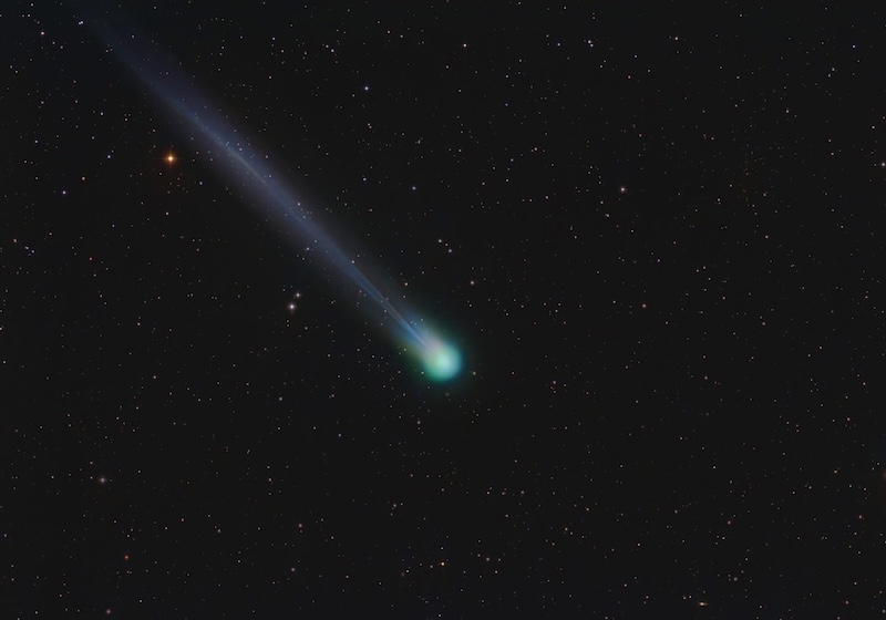 Glowing round, greenish coma of Comet Lemmon with a thin tail streaming away from it.