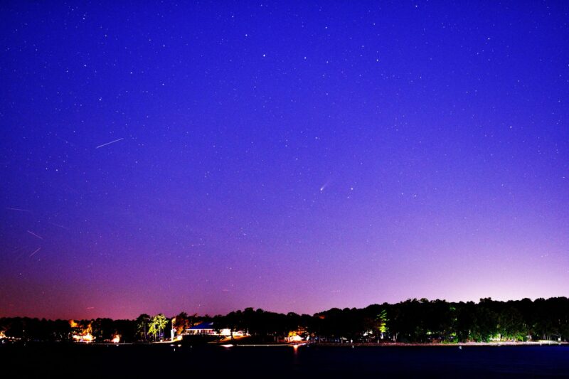 Cobalt blue sky, pink along the horizon, with many stars and a small, fuzzy comet at center.
