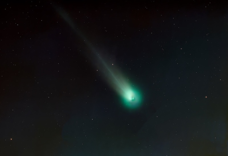 Several small glowing bits inside a fuzzy green head of a comet with a short greenish tail.