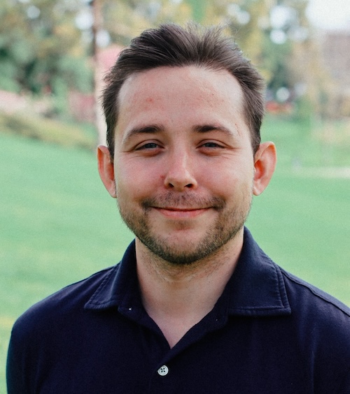 Smiling man with scruffy beard and moustache, wearing a dark blue shirt.