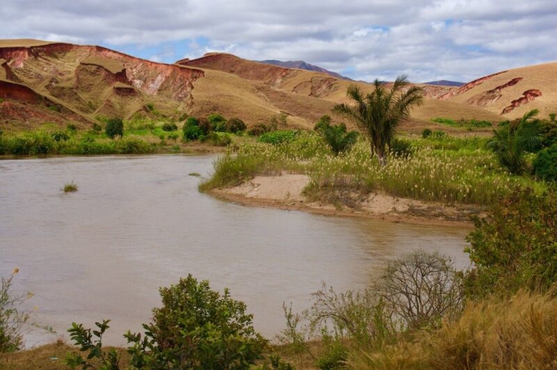 Brown dry hills and a wide, muddy river with some plant life at its brinks.
