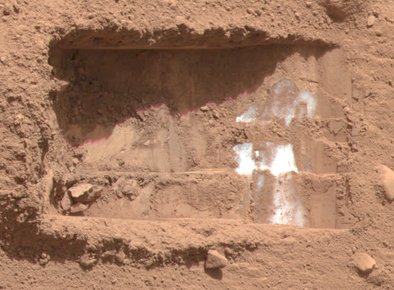 Microbes on Mars: Rectangular trench dug into brownish sand. A few spots of bright white ice are on the bottom of the trench, on the right side.