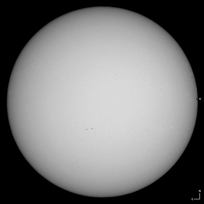 The sun, seen as a large white sphere with small dark spots.