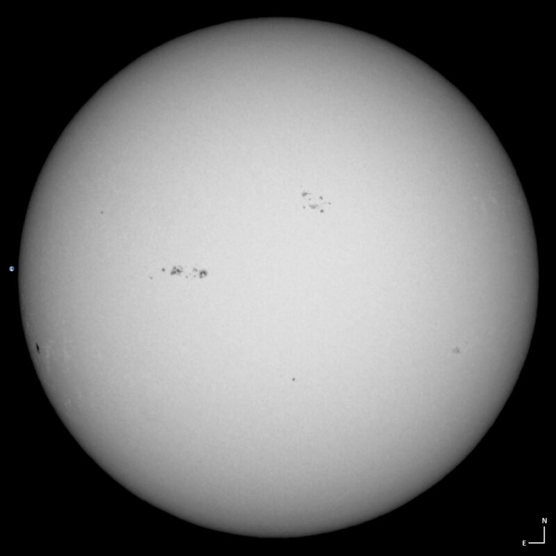 The sun, seen as a large white sphere with small dark spots.