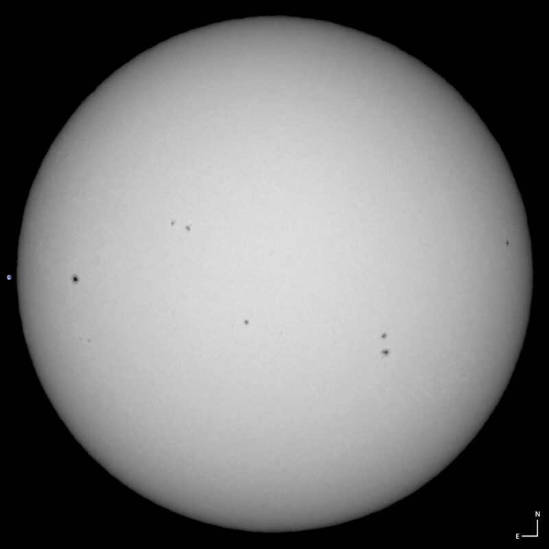 The sun, seen as a large white sphere with small dark spots.