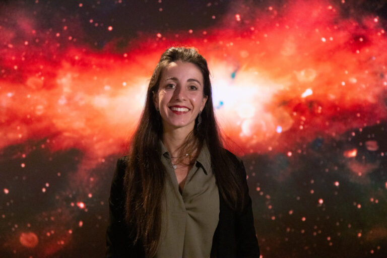 A young woman with long dark hair standing in front of the Milky Way radio image.