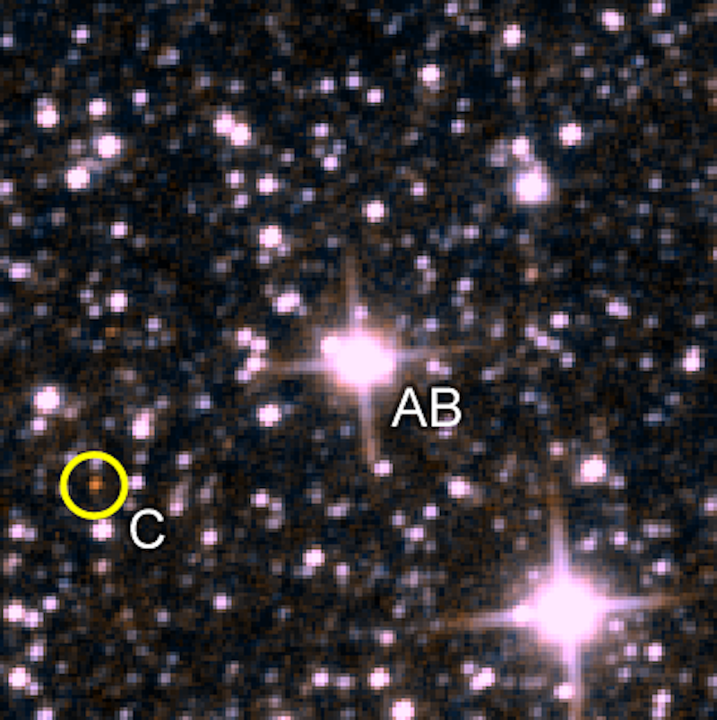 2 bright stars, one marked AB, and a faint reddish star in a yellow ring marked C. More stars are in the background.