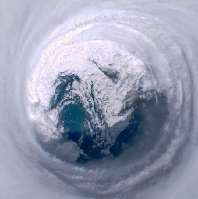 View looking down into tight spiral clouds around a clear center with water visible in it.