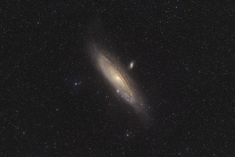 A vast, yellowish disk and tight spiral arms of a galaxy with sparse foreground stars.