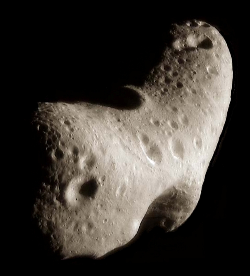Closeup of a lumpy, irregular asteroid in space. It is white and gray, with many craters.