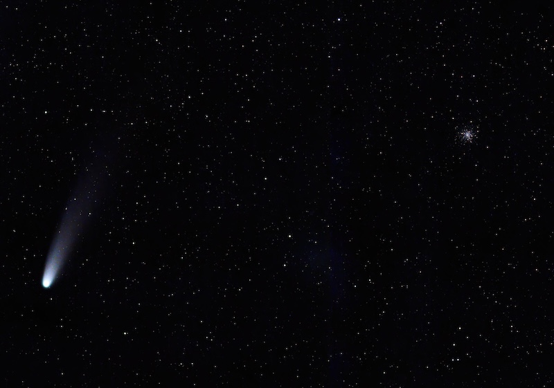 A fuzzy comet to the left in a starry sky, with a cluster of stars to the right.