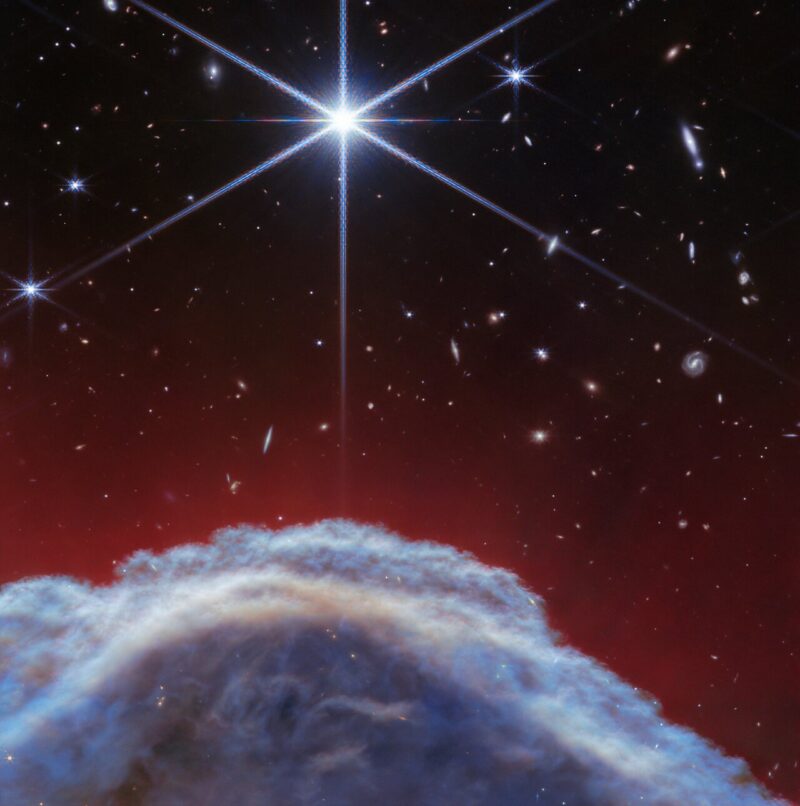 White dust looking like an Earth cloud below a very bright star with 6 rays, and background stars and galaxies.