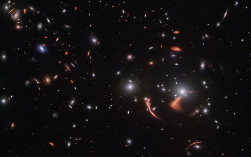 Very many tiny bright oblongs with thin, smeared arcs of light surrounding one cluster of them.