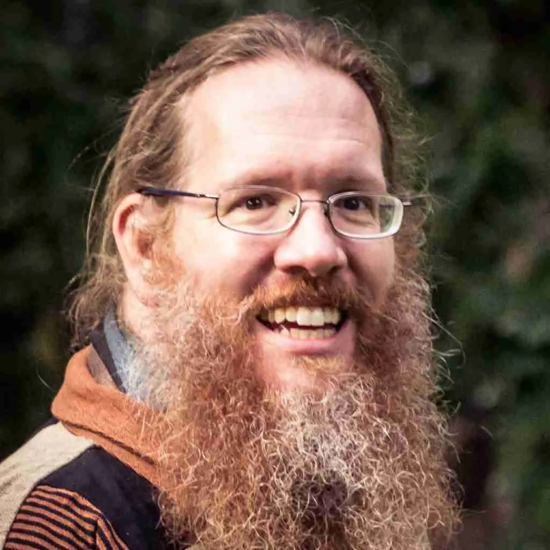 A man with glasses and hair swept bag and a large, full beard.