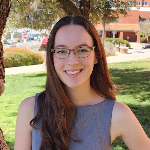 Smiling woman with long hair and eyeglasses wearing a light blue sleeveless shirt.