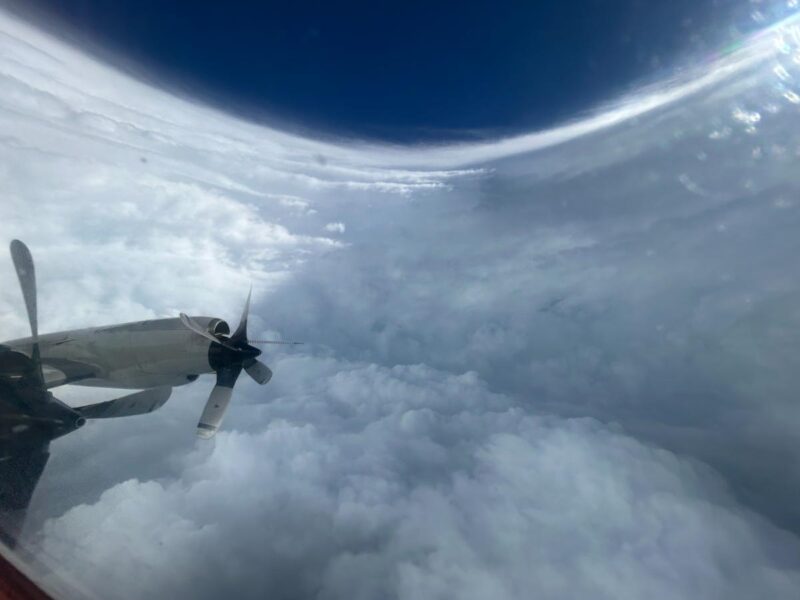 Interior view of a tall, curved wall of clouds under a blue sky with airplane propeller nacelle in view.