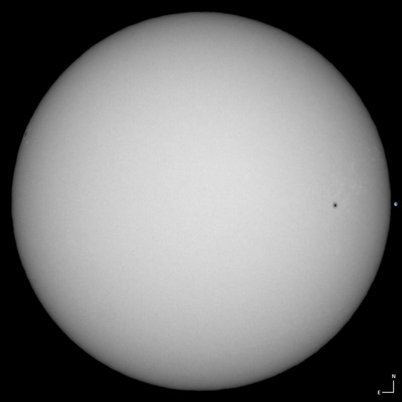 The sun, seen as a large white sphere with small dark spots.
