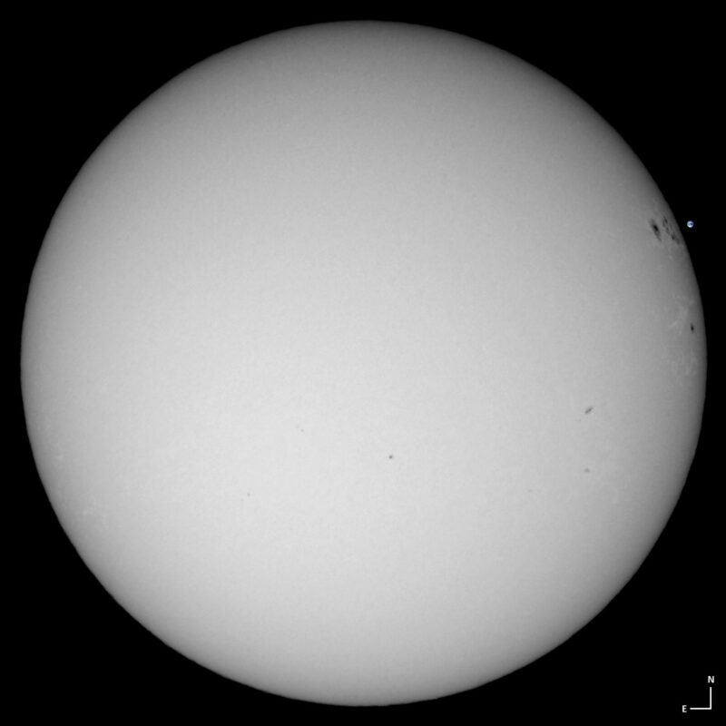 The sun, seen as a large white sphere with small dark spots.