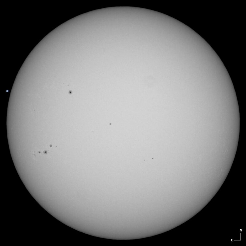 The sun, seen as a large white sphere with small dark spots.