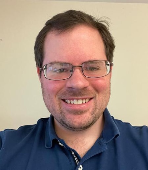 Smiling man with eyeglasses wearing a blue shirt.