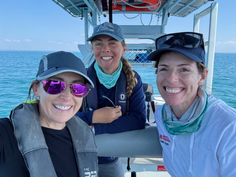 3 women on a boat smiling and looking at the camera.