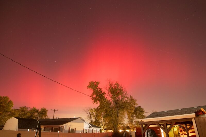 A wide-angle view at night with a diffuse red light in the sky and a house in the foreground.