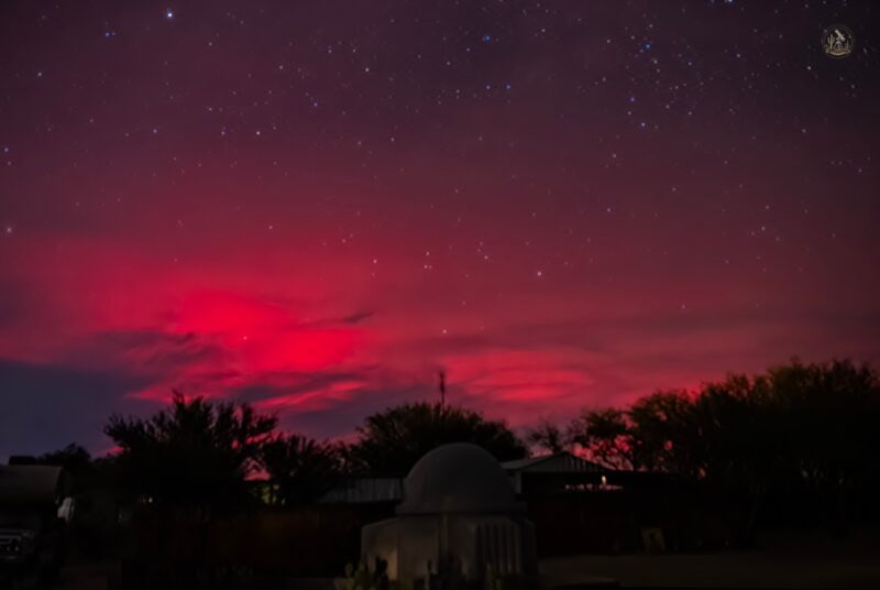 A small observatory on the ground, the sky covered with a pink light and many blue and white stars.