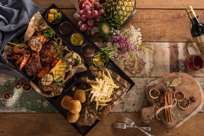 Overeating: A spread of food including rolls, meats, fruit, french fries and wine.