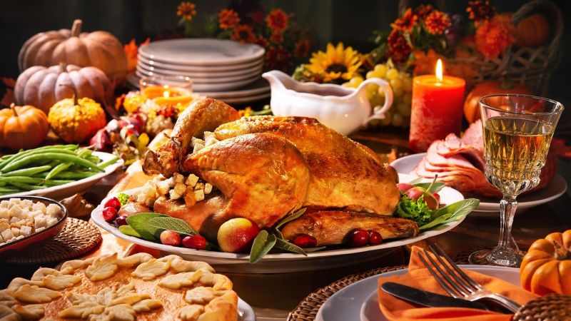 A whole roast turkey and many side dishes on a table decorated for the holiday with small squashes and a candle.