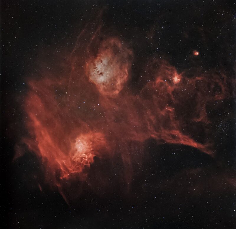 A complex structure of red gas overlaid with small dark patches, with numerous background stars.