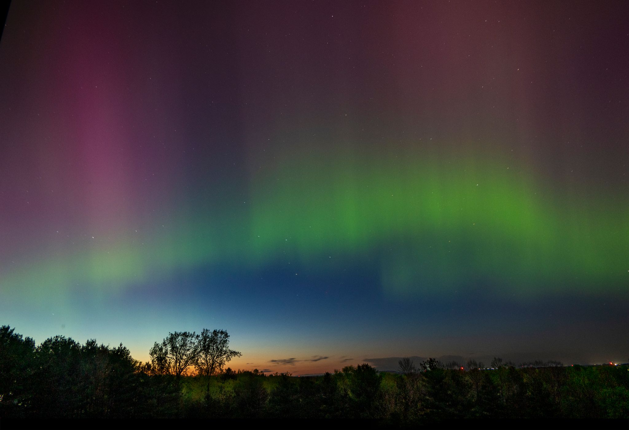 Green at the bottom and pink at top, a folding arc of northern lights over a dark landscape.