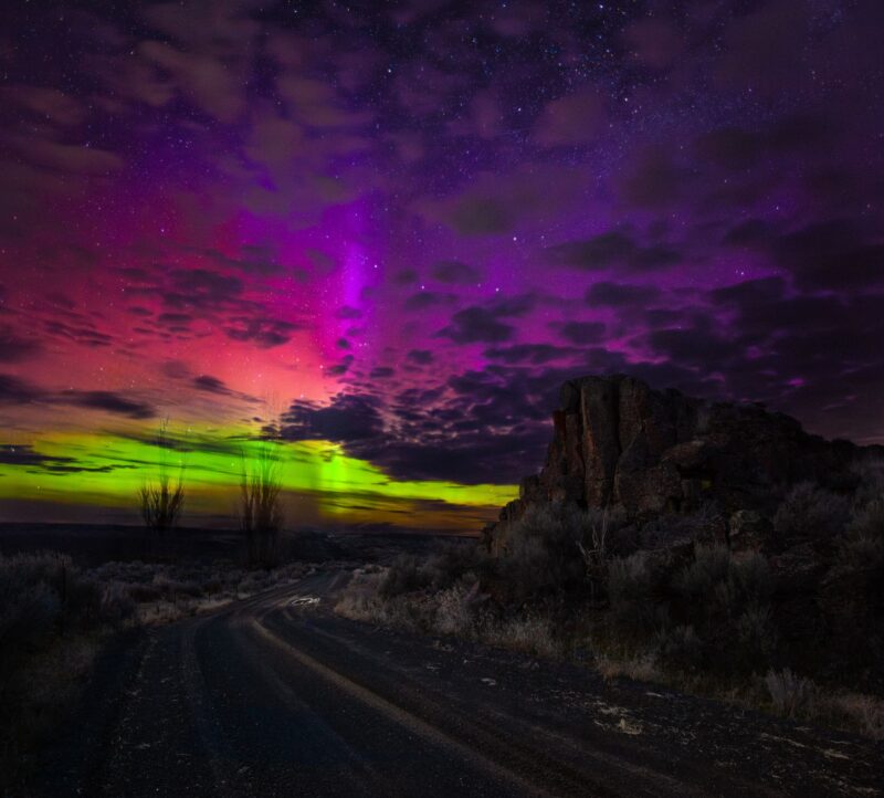 Forms of aurora: Rainbow colors of light on the sky, with dark clouds blocking patches and a dark rural landscape.