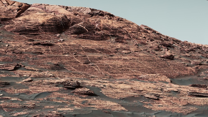 Mountainous rocky ridge in brown terrain, with dusty bluish sky in background.