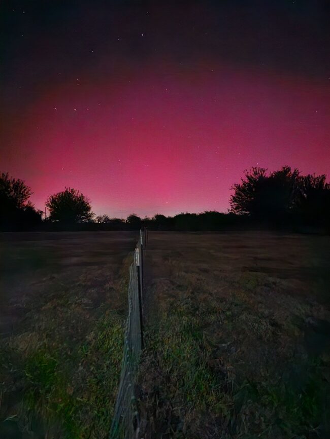 A reddish glow brightens the horizon of a dark rural landscape.