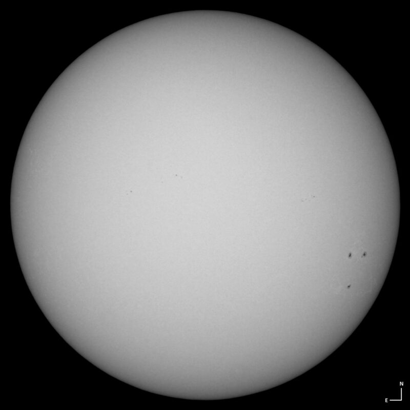 The sun, seen as a large white sphere with small dark spots.