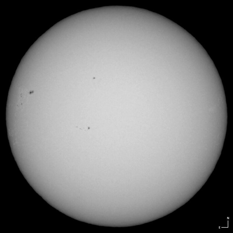 The sun, seen as a large white sphere with small dark spots.