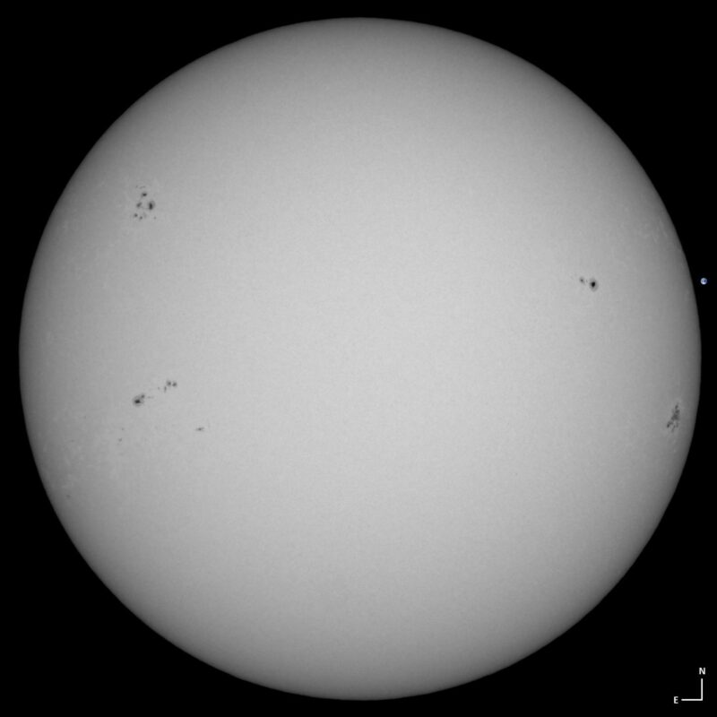 The sun, seen as a large white sphere with small dark spots.