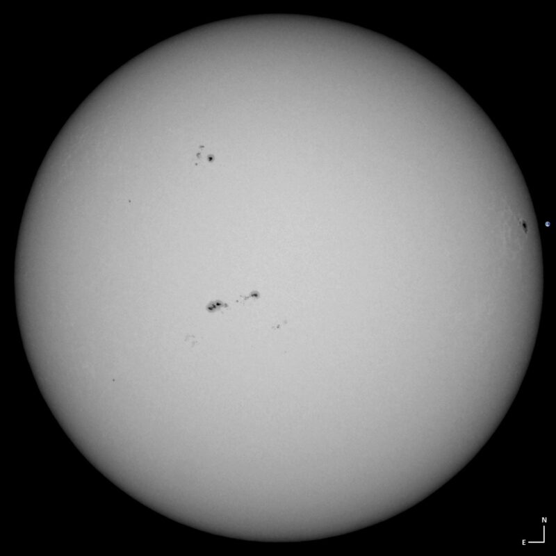 The sun, seen as a large white sphere with small dark spots.