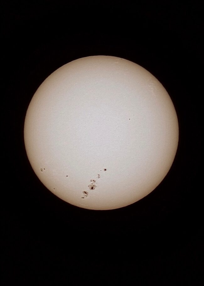 The sun, seen as a large white sphere with small dark spots.