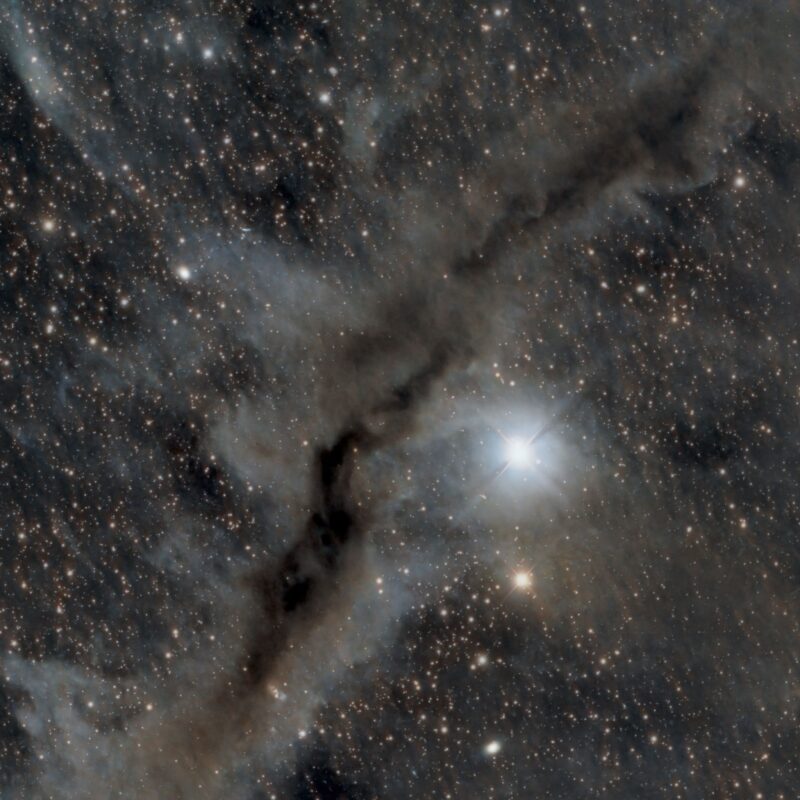 A complex structure of whitish gas bisected by a dark dust lane, with numerous background stars.