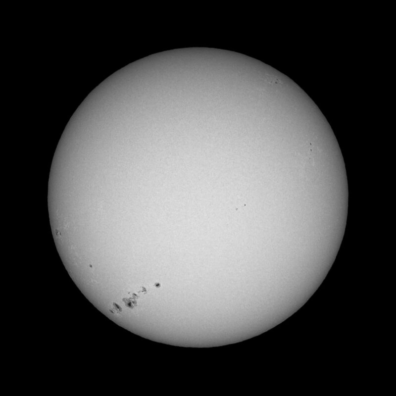 The sun, seen as a large white sphere with small dark spots.