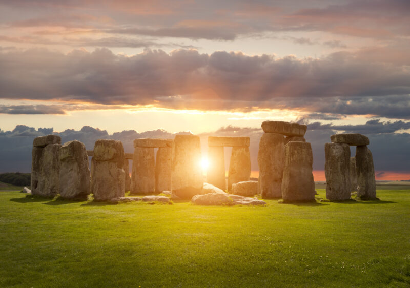 Big, rectangular stones standing in a circle, with the sun shining between them.