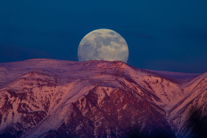 A full moon peeking out behind a mountain.