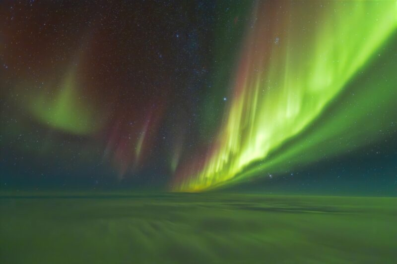 Clouds below and green and red curtains of aurora above.